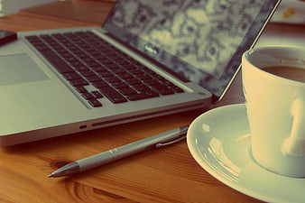 Laptop, coffee cup, and pen on wooden desk workspace