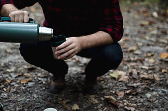 Man pouring hot coffee from thermos in autumn forest
