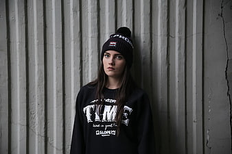 Woman in black beanie and sweatshirt against concrete wall