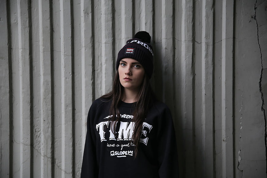 Woman in black beanie and sweatshirt against concrete wall