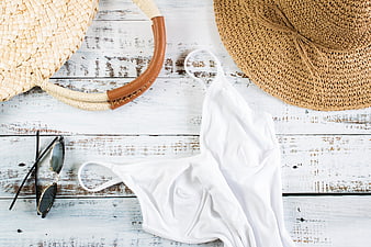 Summer vacation flat lay with white swimsuit, straw hat, and sunglasses