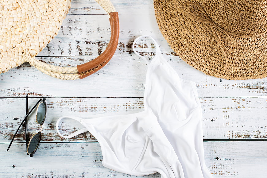 Summer vacation flat lay with white swimsuit, straw hat, and sunglasses