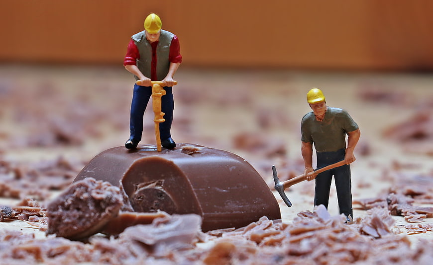 Miniature construction workers mining chocolate with jackhammer and pickaxe