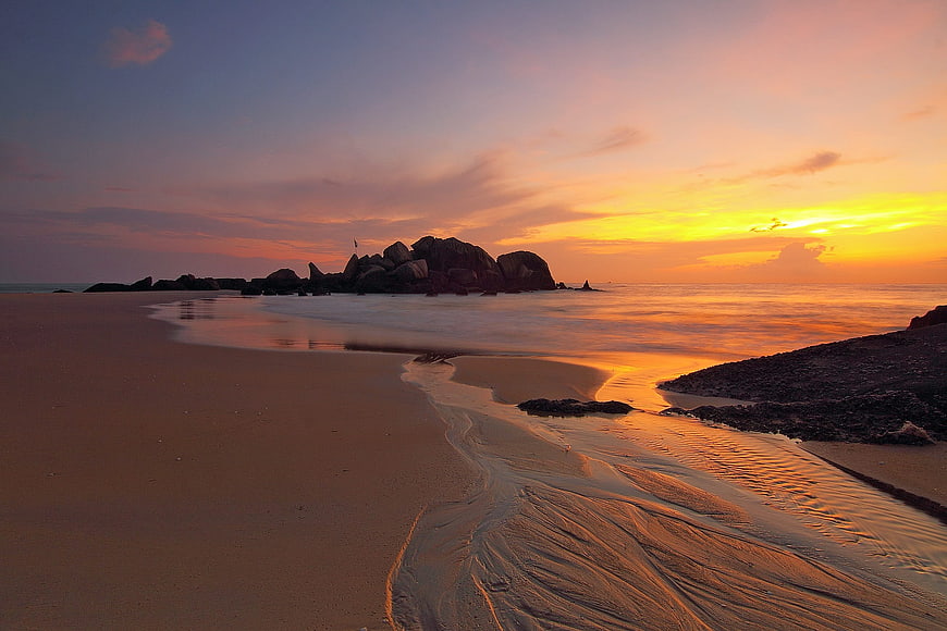 Serene Sunset Seascape with Rock Formations and Sandy Beach