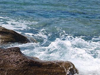 Ocean waves crashing against dark rocks on a sunny day