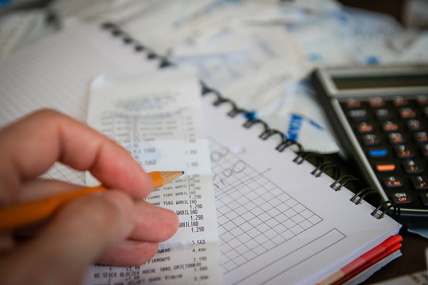 Hand holding pencil over receipt and calculator on notebook