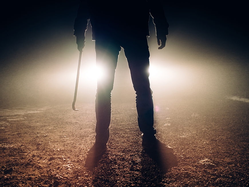 Silhouette of menacing figure holding crowbar in foggy night