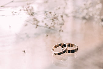 Two Gold Wedding Rings on Glass Table with Flowers