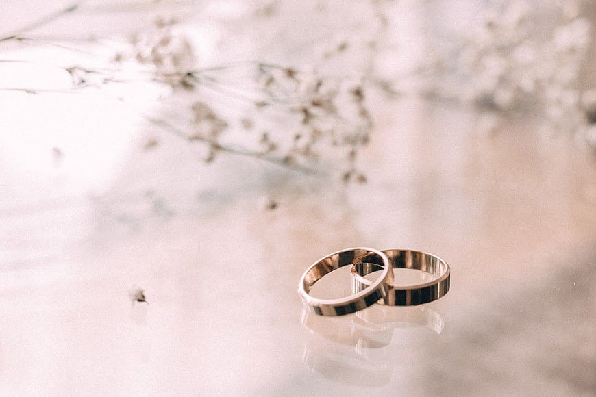 Two Gold Wedding Rings on Glass Table with Flowers
