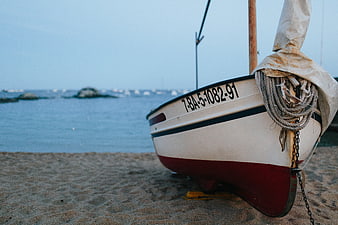 White and red sailboat on sandy beach with ocean background
