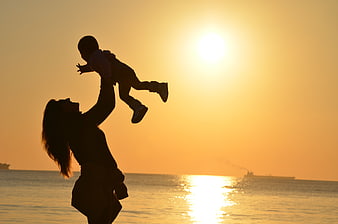 Silhouette of Mother Lifting Baby at Sunset Beach