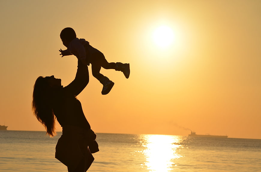 Silhouette of Mother Lifting Baby at Sunset Beach