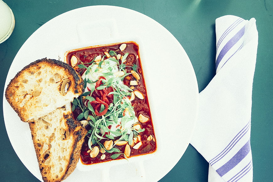 Overhead view of spicy shakshuka with toasted bread on teal table