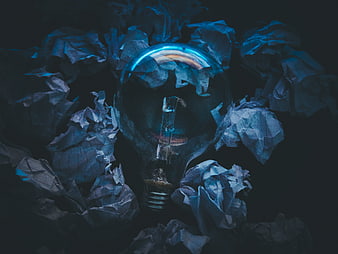 Light bulb surrounded by crumpled paper in dark blue lighting