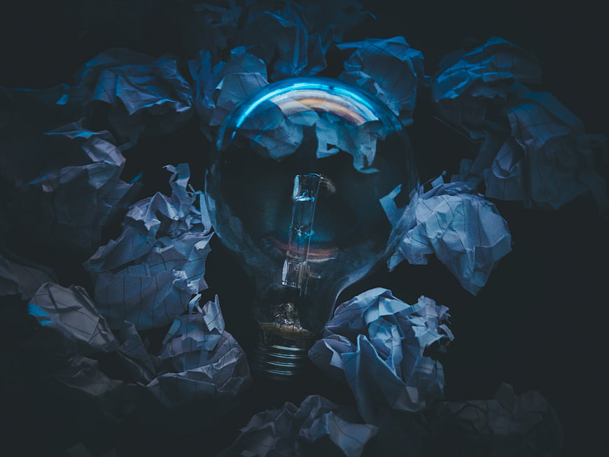 Light bulb surrounded by crumpled paper in dark blue lighting