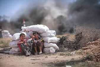 Two boys smiling behind sandbags with smoke in background