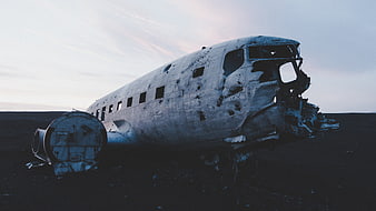 Crashed airplane wreck on black sand beach at dusk
