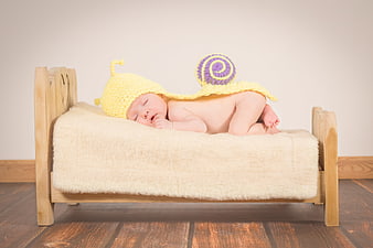 Sleeping newborn baby in yellow snail costume on miniature wooden bed