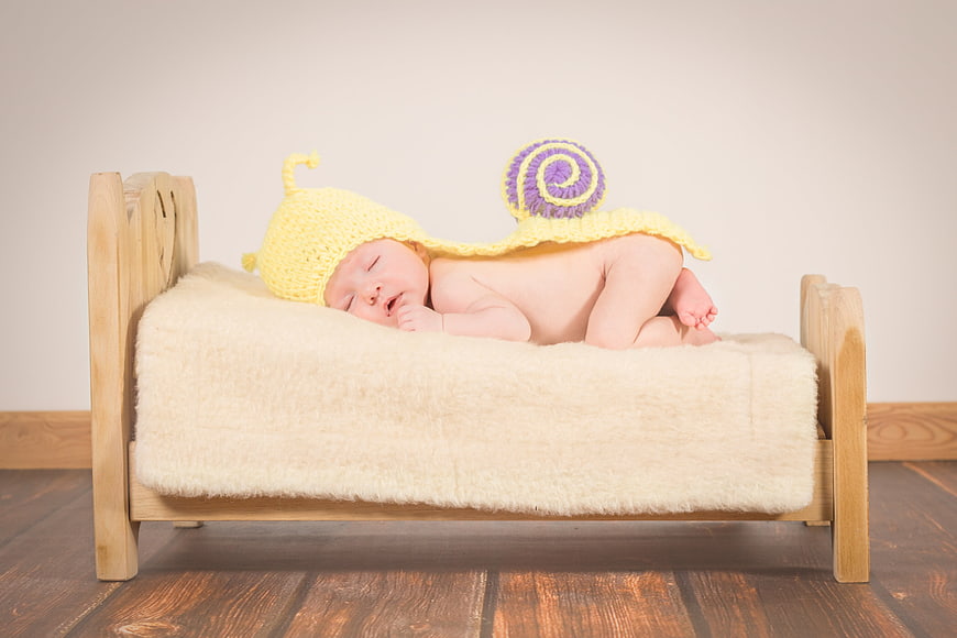 Sleeping newborn baby in yellow snail costume on miniature wooden bed