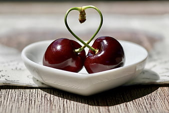 Two cherries with heart-shaped stems in a white bowl