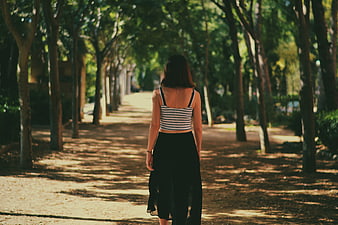 Woman Walking Away on Tree-Lined Path in Park