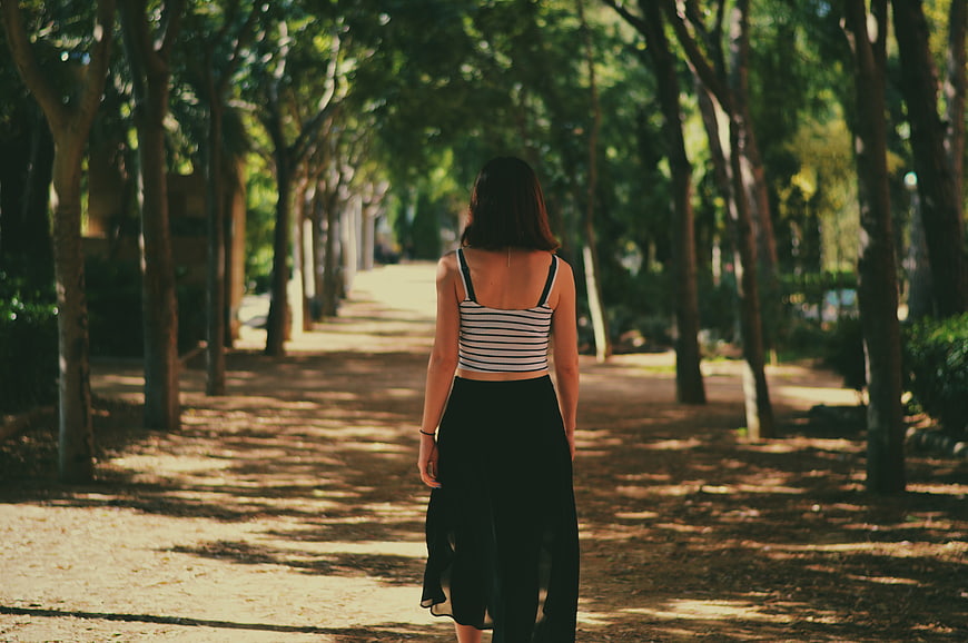 Woman Walking Away on Tree-Lined Path in Park
