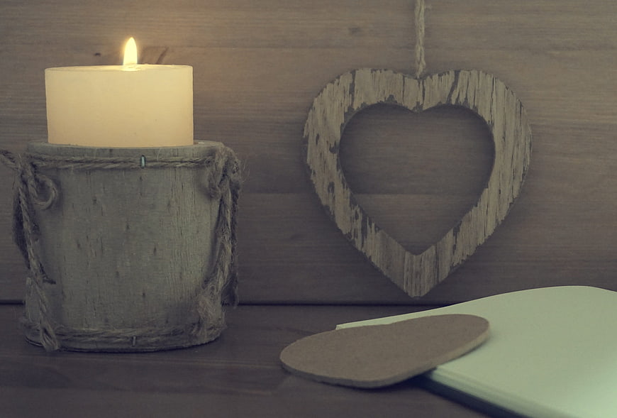 Rustic wooden heart and candle on table with notebook