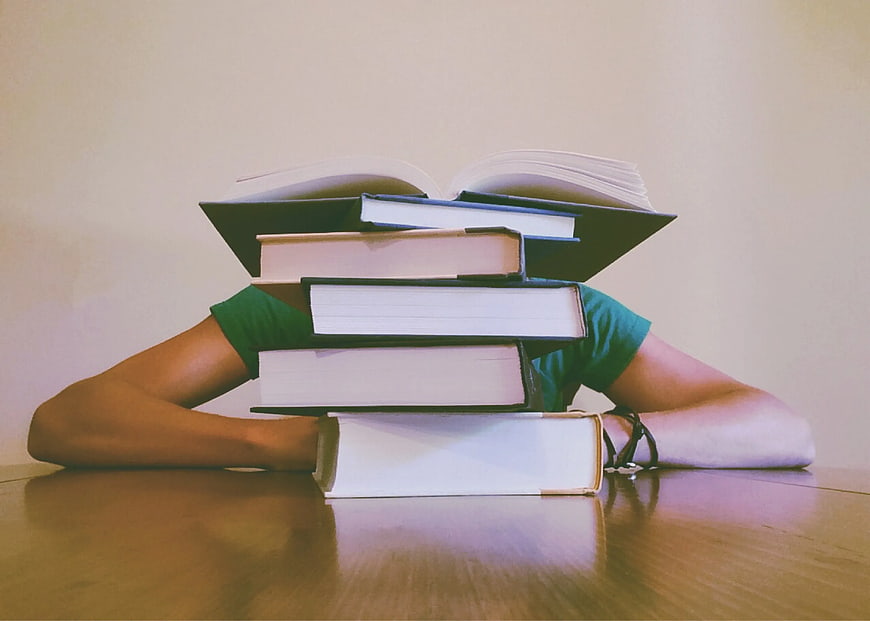 Student buried under stack of books studying