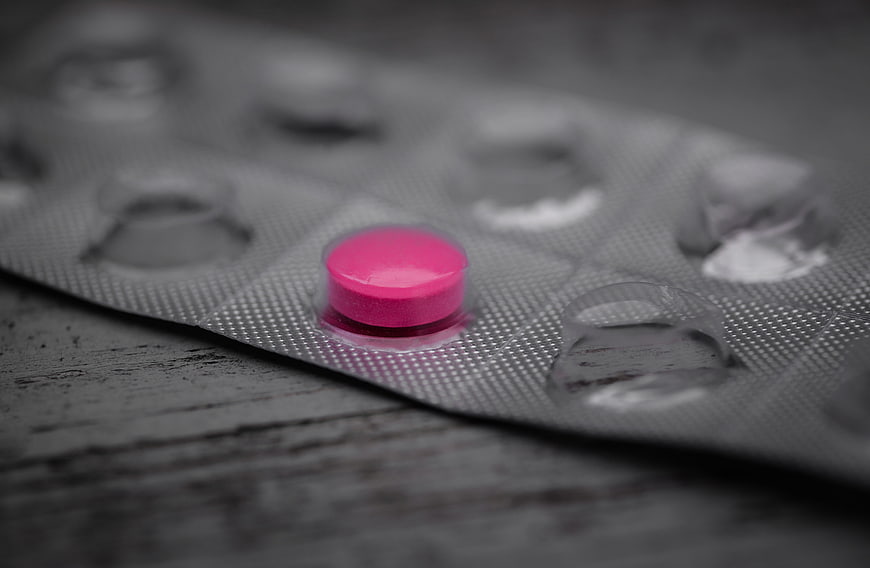 Single pink pill in blister pack on dark wooden surface