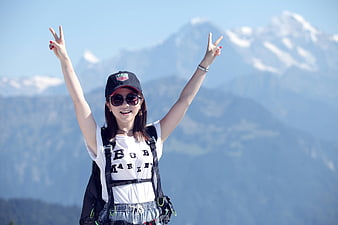 Happy female hiker with backpack and peace signs in front of mountains