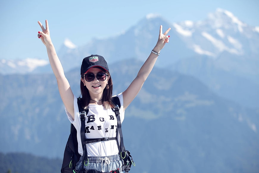 Happy female hiker with backpack and peace signs in front of mountains