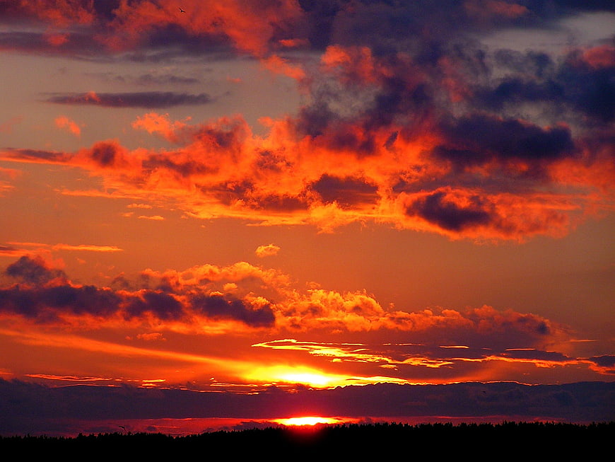 Dramatic fiery orange sunset sky with clouds over silhouette