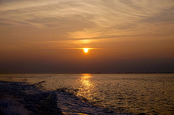 Golden sunset over ocean with boat wake and distant horizon