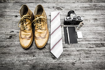 Vintage leather shoes, tie, and camera on rustic wood