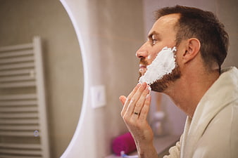 Man applying shaving cream in bathroom mirror