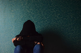 Woman in black hoodie sitting against textured teal wall