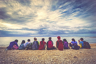 Group of friends with backpacks sitting on pebble beach