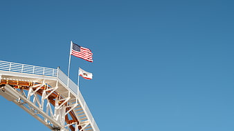 American and California flags on white structure against blue sky