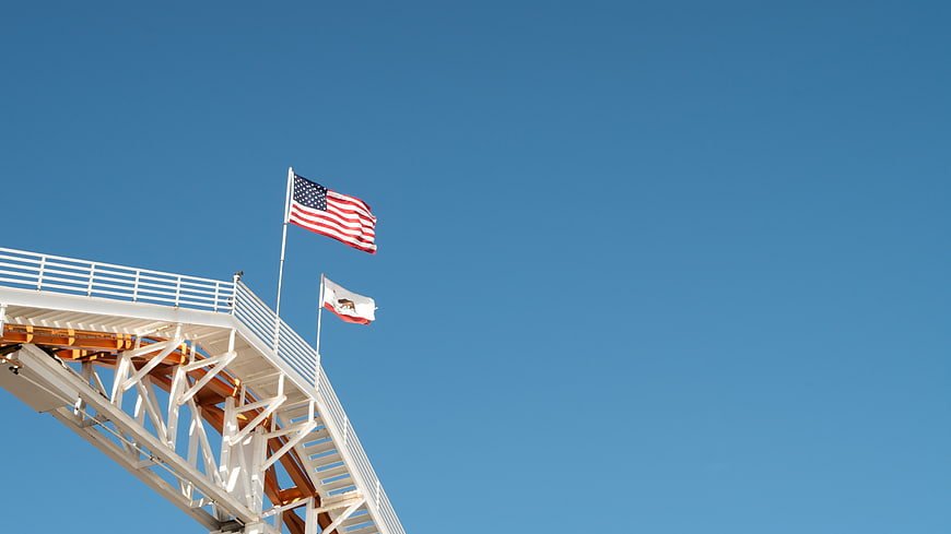 American and California flags on white structure against blue sky