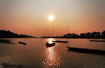 Silhouetted boats on river at golden sunset