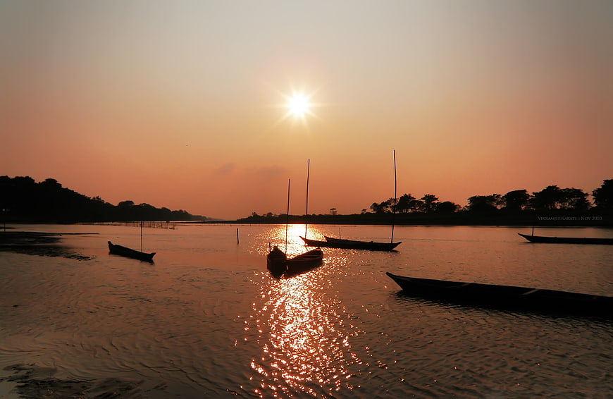 Silhouetted boats on river at golden sunset