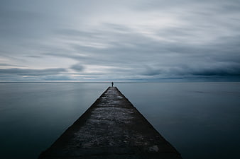 Solitary Figure Standing on Pier Under Moody Cloudy Sky