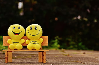 Two yellow smiley plush toys sitting on a miniature wooden bench