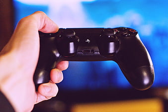Hand Holding Black PlayStation Controller with Blue Background