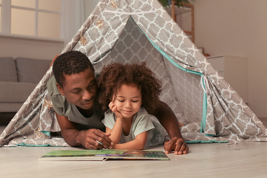 Father and daughter reading together in a play tent