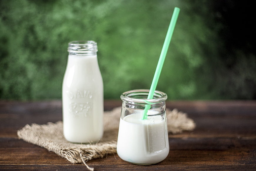 Fresh milk in glass bottle and jar with green straw on rustic wood