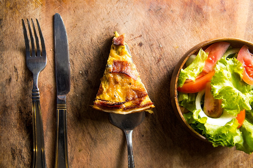 Quiche slice with salad on rustic wooden table
