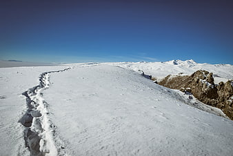 Snowy mountain trail with footprints leading to distant peaks