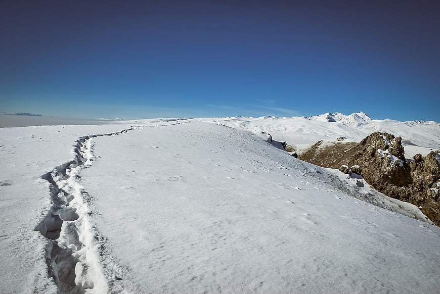 Snowy mountain trail with footprints leading to distant peaks