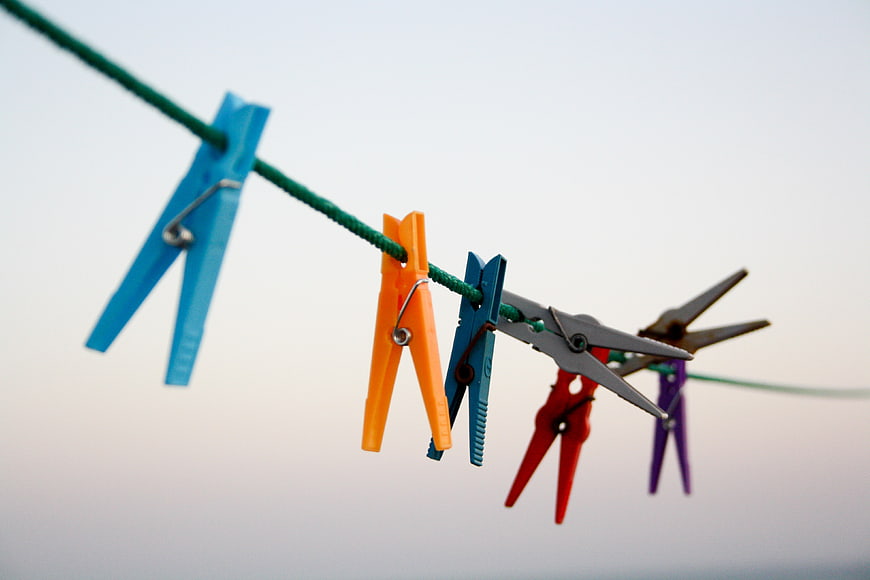 Colorful clothespins hanging on a green rope against a white background